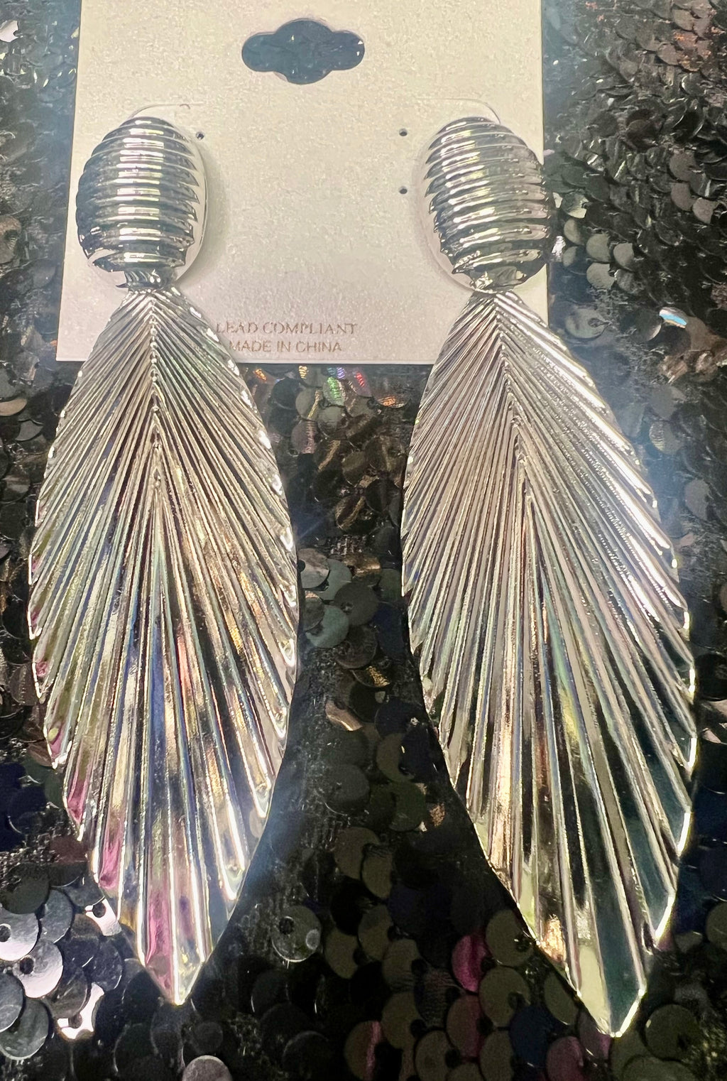 Silver feather-shaped earrings on a sequined background
