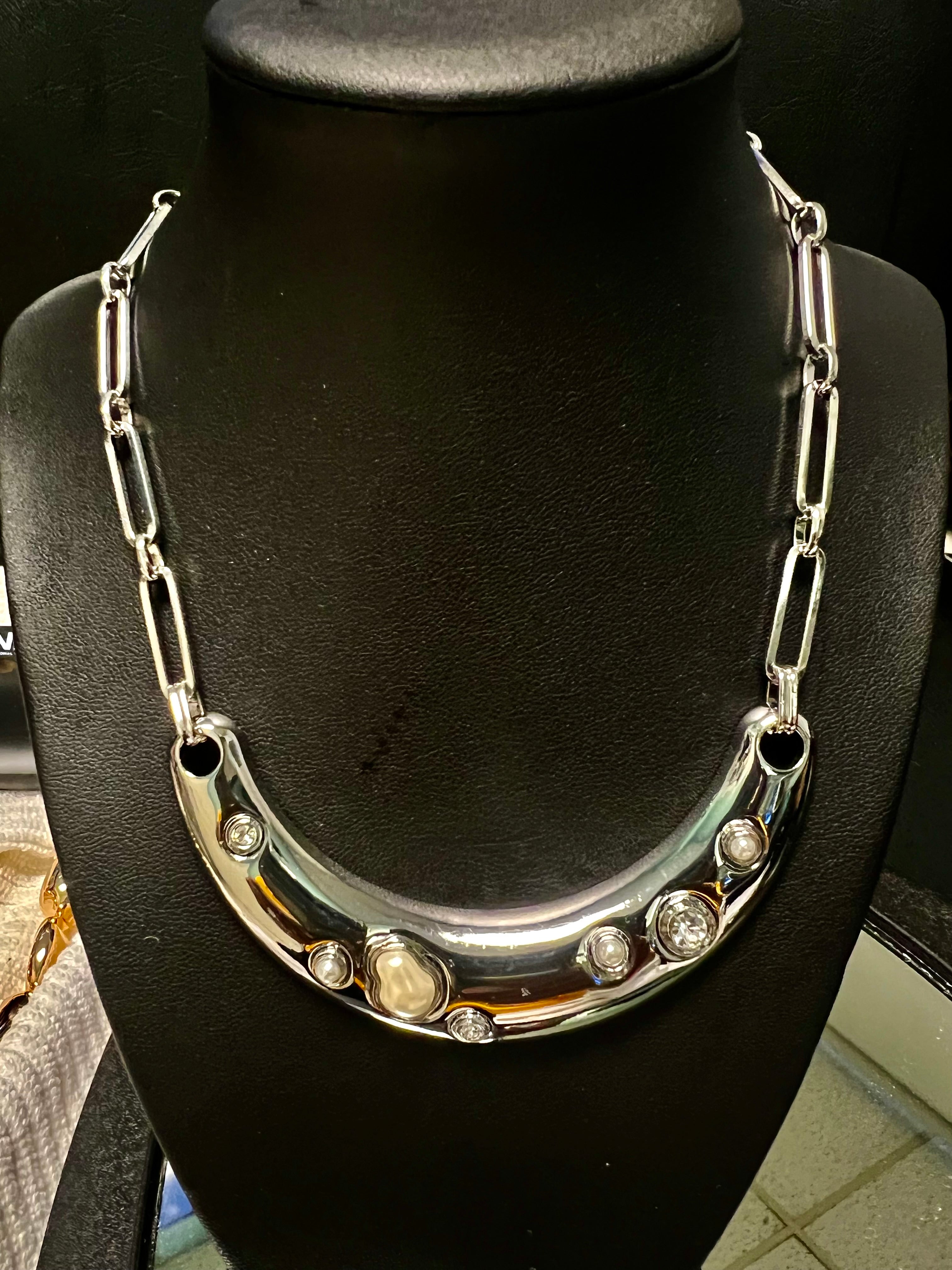 Silver necklace with embedded stones on a black stand