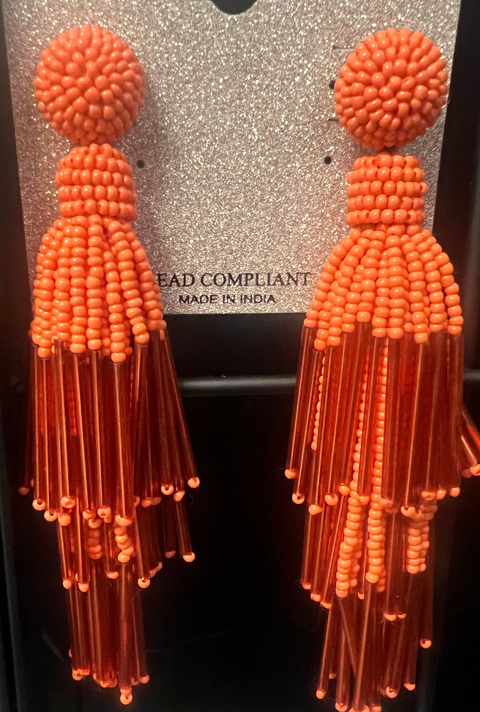 Pair of orange beaded tassel earrings on a card with text.