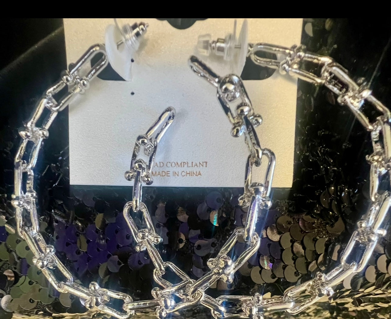 Silver chain hoop earrings on a black sequin background